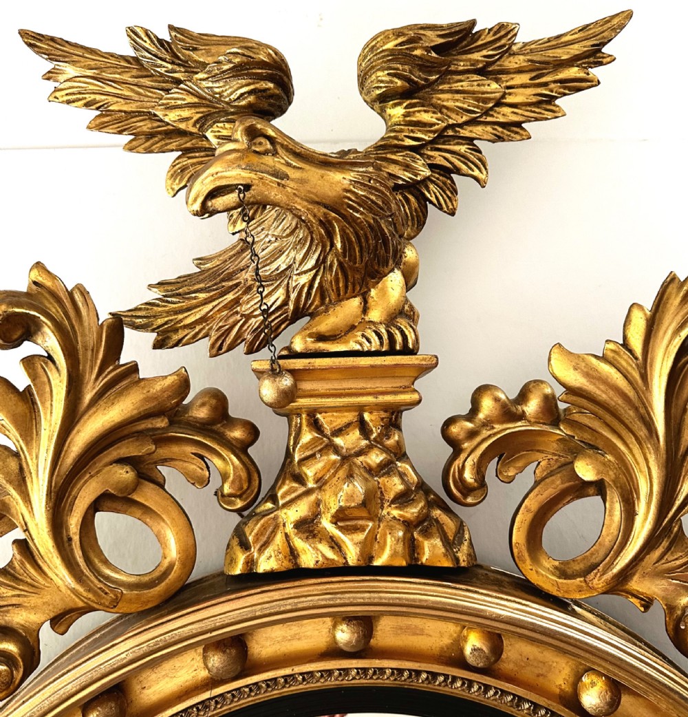 A circular Regency giltwood convex mirror featuring a carved eagle cresting, acanthus leaf scrolls, and ball mouldings around an ebonised inner slip. View IV