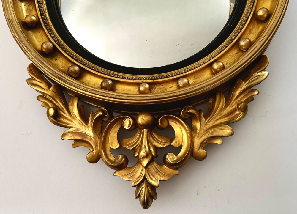 A circular Regency giltwood convex mirror featuring a carved eagle cresting, acanthus leaf scrolls, and ball mouldings around an ebonised inner slip. View V