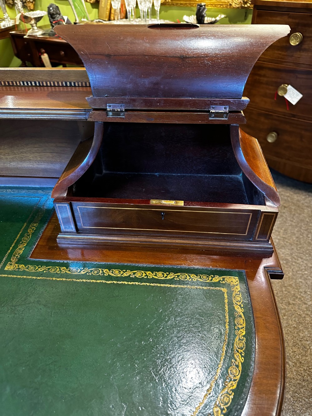 An antique mahogany writing desk featuring a green leather surface, a raised central superstructure with small drawers, satinwood string inlay, and tapered legs on brass castors. View VII