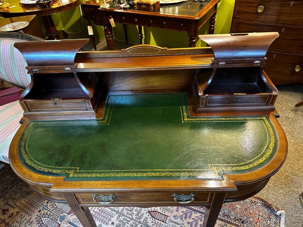 An antique mahogany writing desk featuring a green leather surface, a raised central superstructure with small drawers, satinwood string inlay, and tapered legs on brass castors. View VIII