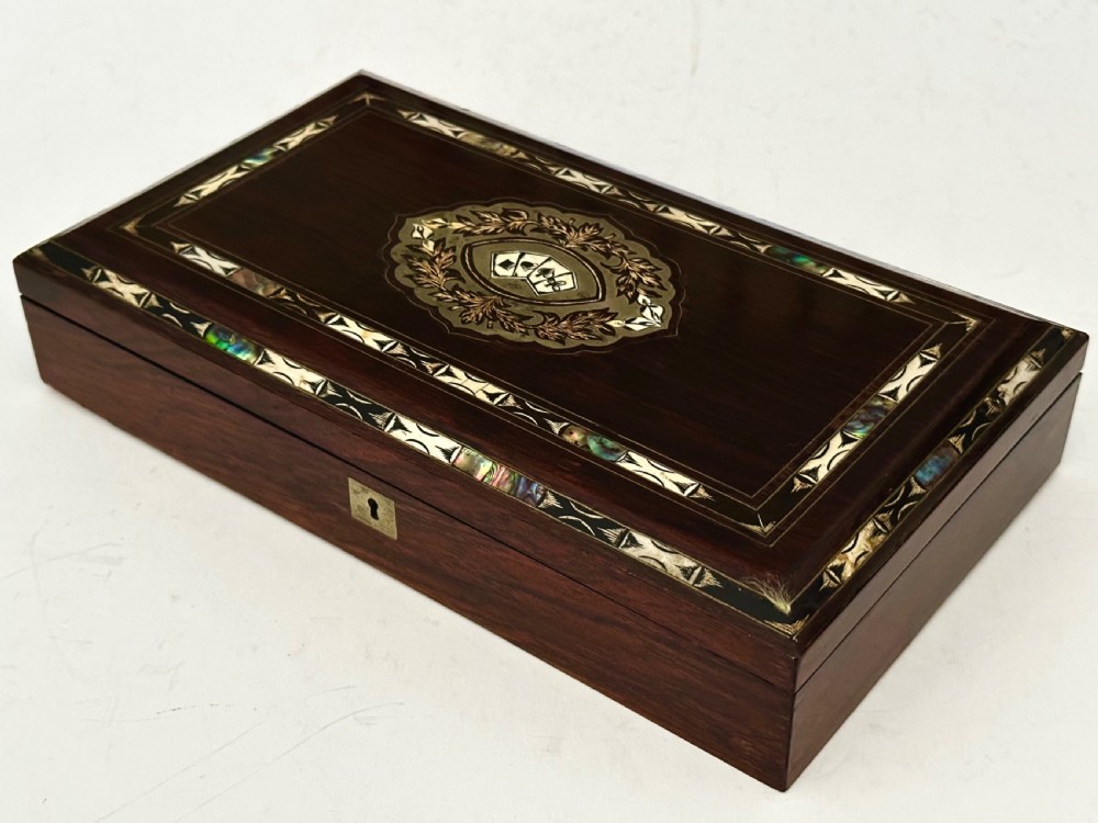 A rectangular dark rosewood games box featuring mother-of-pearl and abalone inlaid borders with a central playing card motif medallion and a brass keyhole.