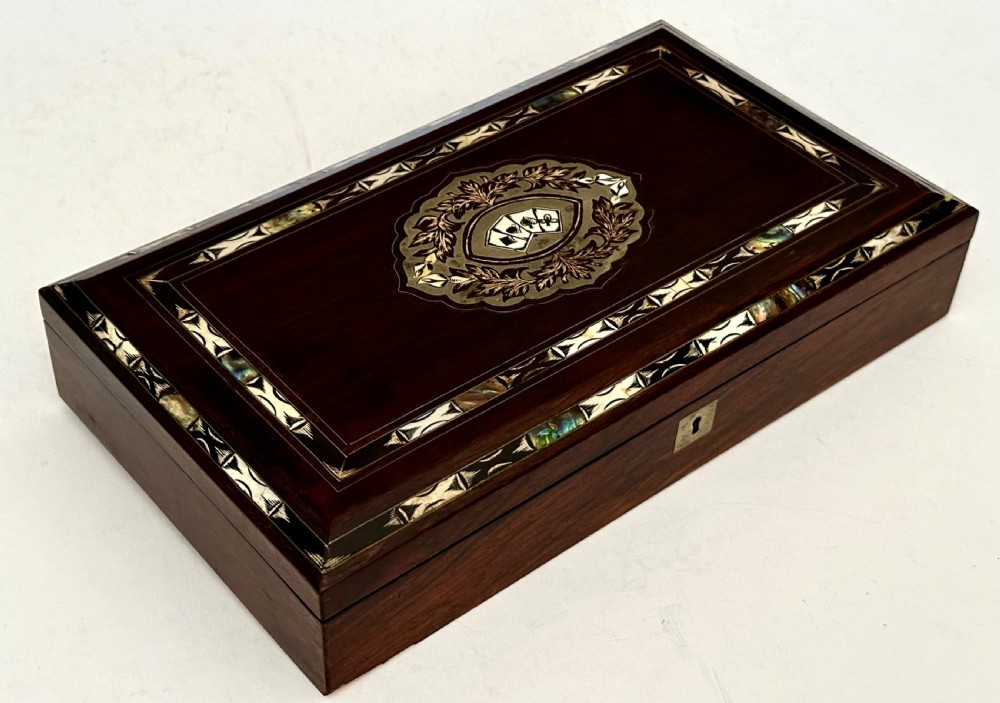 A rectangular dark rosewood games box featuring mother-of-pearl and abalone inlaid borders with a central playing card motif medallion and a brass keyhole. View II