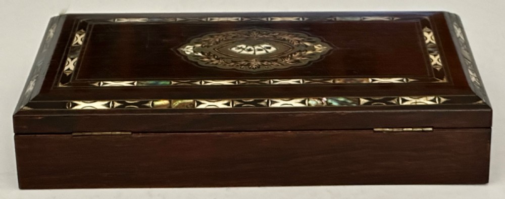 A rectangular dark rosewood games box featuring mother-of-pearl and abalone inlaid borders with a central playing card motif medallion and a brass keyhole. View IV