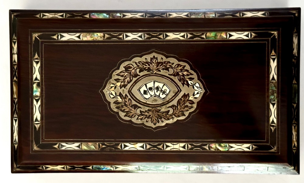 A rectangular dark rosewood games box featuring mother-of-pearl and abalone inlaid borders with a central playing card motif medallion and a brass keyhole. View X