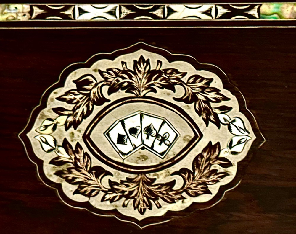 A rectangular dark rosewood games box featuring mother-of-pearl and abalone inlaid borders with a central playing card motif medallion and a brass keyhole. View XII