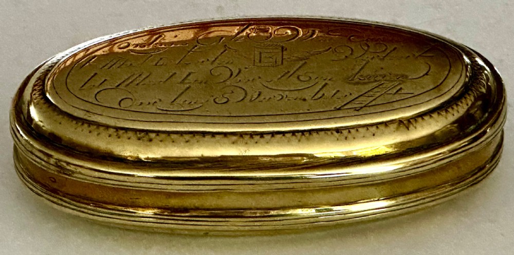 An 18th-century oval brass tobacco box featuring hand-engraved Dutch calligraphy and a hinged lid. View II