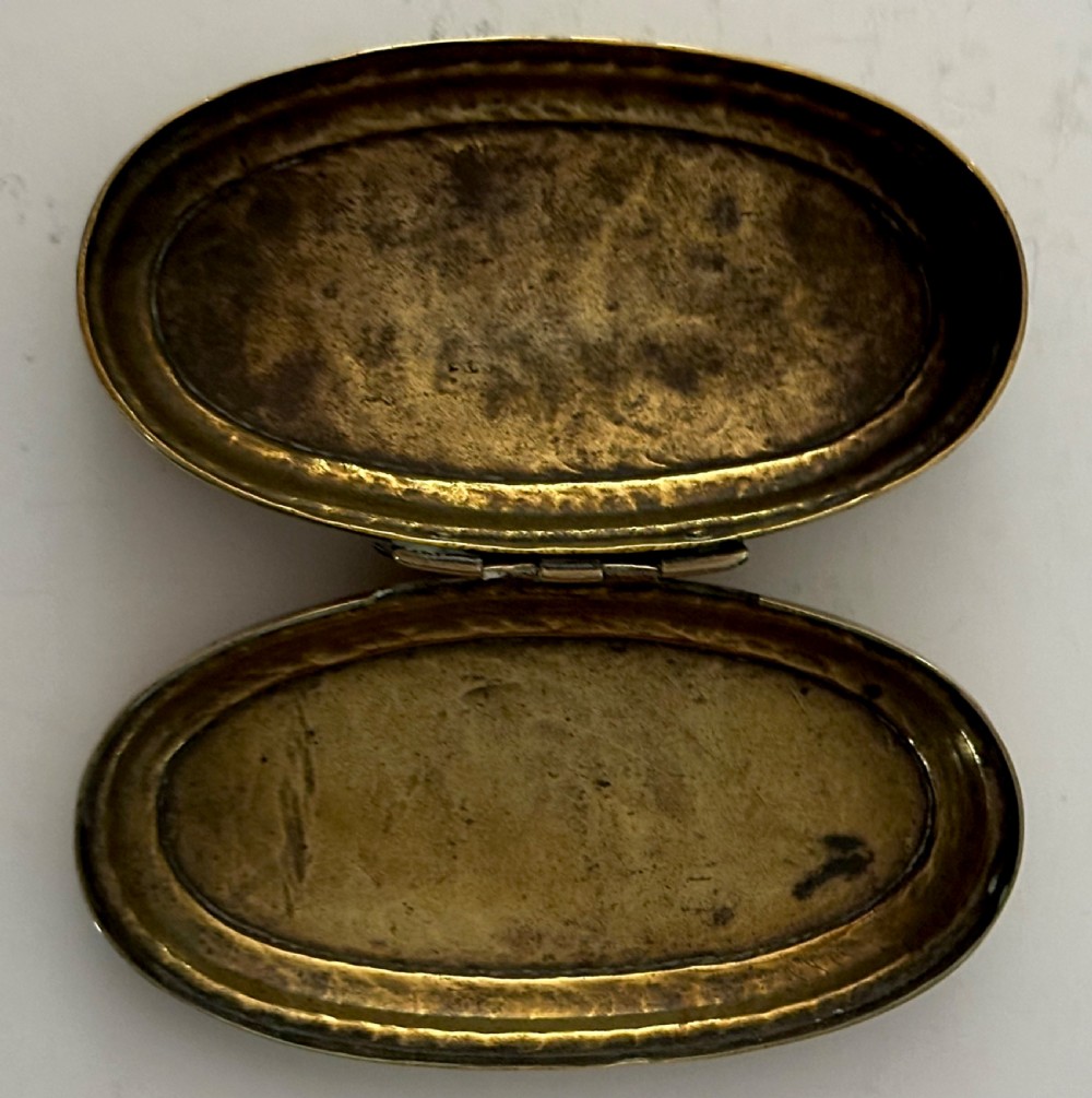 An 18th-century oval brass tobacco box featuring hand-engraved Dutch calligraphy and a hinged lid. View V