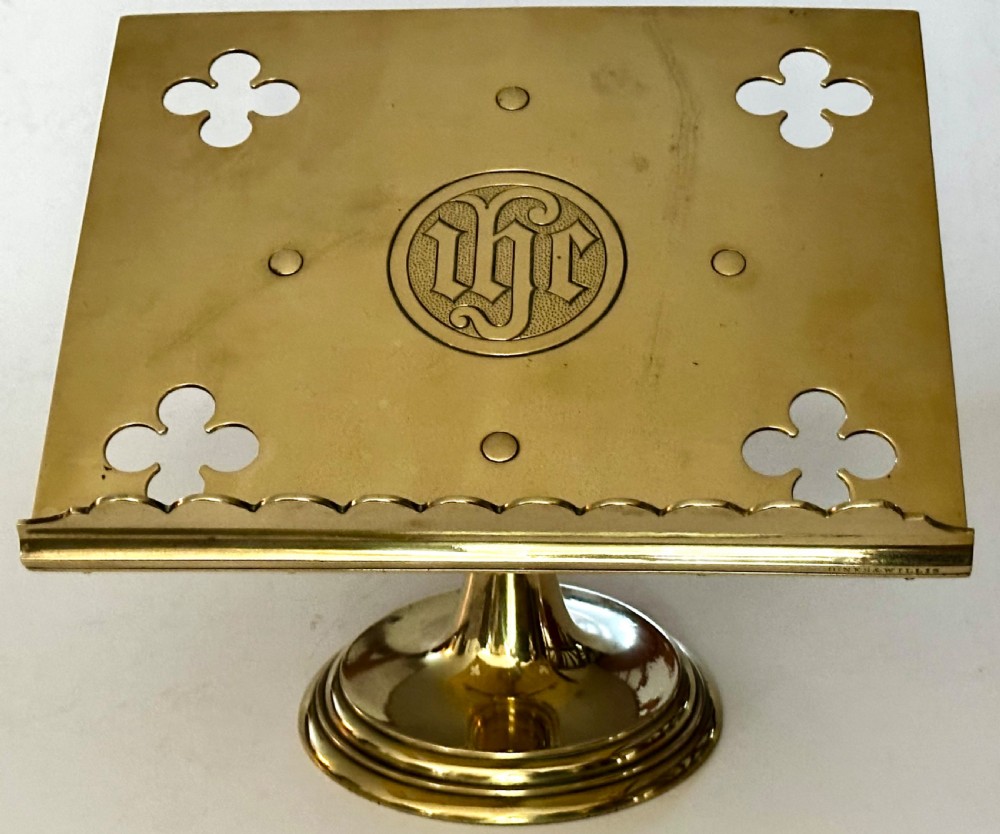 A polished brass tabletop lectern featuring quatrefoil corner cutouts, an engraved Gothic monogram inside a central medallion, a scalloped lip, and a stepped circular pedestal base. View II