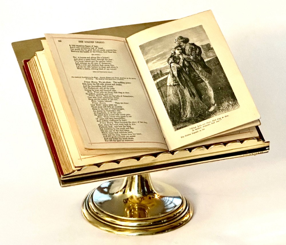 A polished brass tabletop lectern featuring quatrefoil corner cutouts, an engraved Gothic monogram inside a central medallion, a scalloped lip, and a stepped circular pedestal base. View VII
