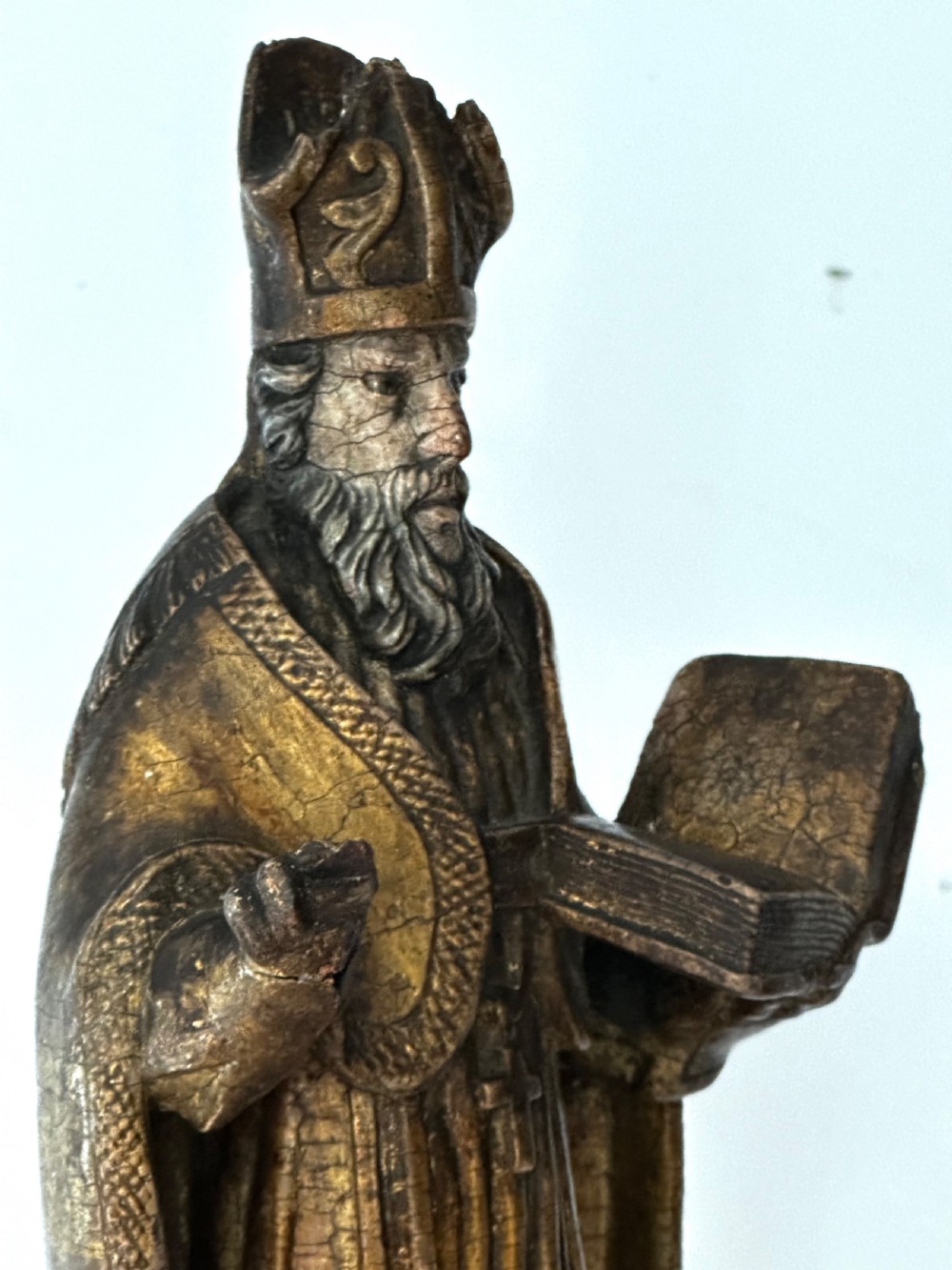 An 18th-century carved wooden statue depicting Saint Nicholas wearing a bishops mitre, holding a cross staff and open book, with aged dark brown and gilt finishes. View VI