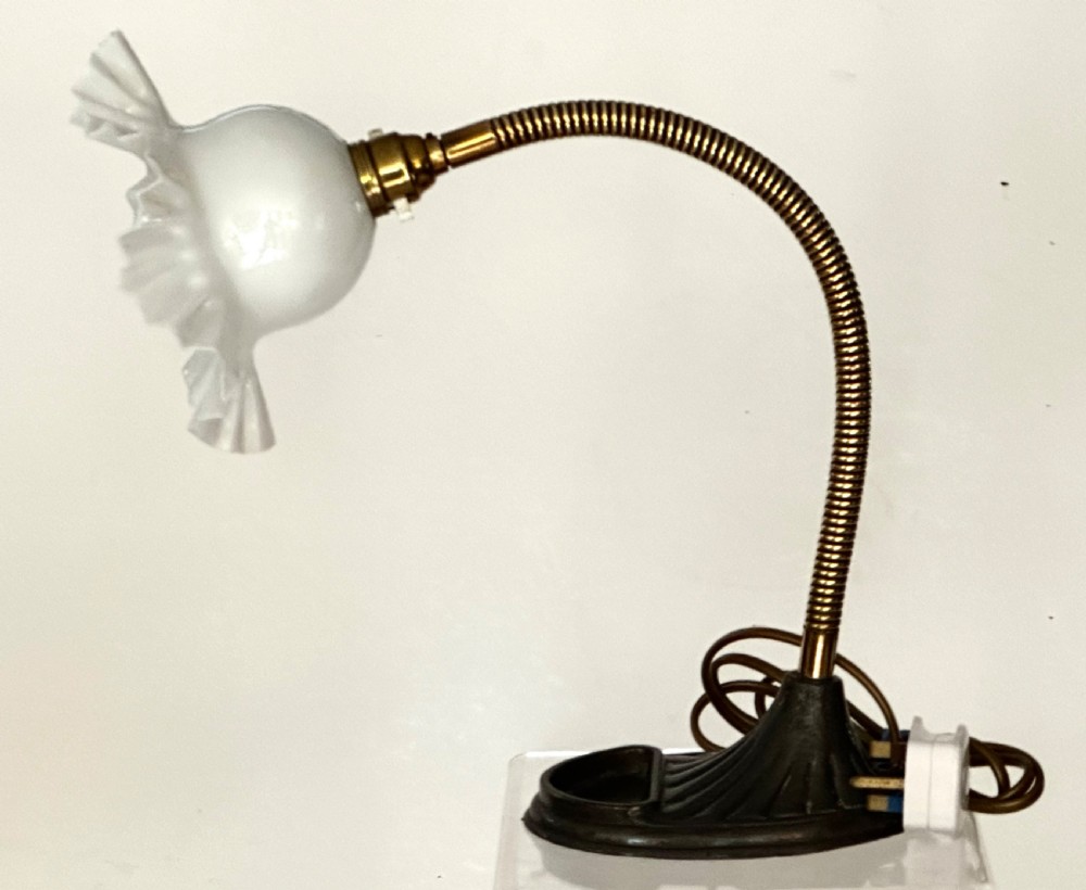 A brass gooseneck desk lamp with a flexible coiled arm, dark cast base featuring a built-in tray, and a ruffled white glass shade.