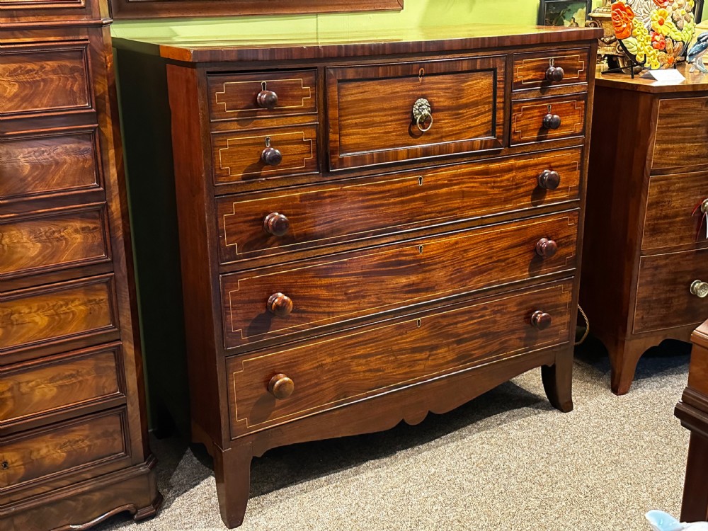 A Regency mahogany Scotch chest of drawers featuring boxwood inlay, a deep central drawer with a brass lion head pull, and multiple outer drawers with turned wooden knobs. View II