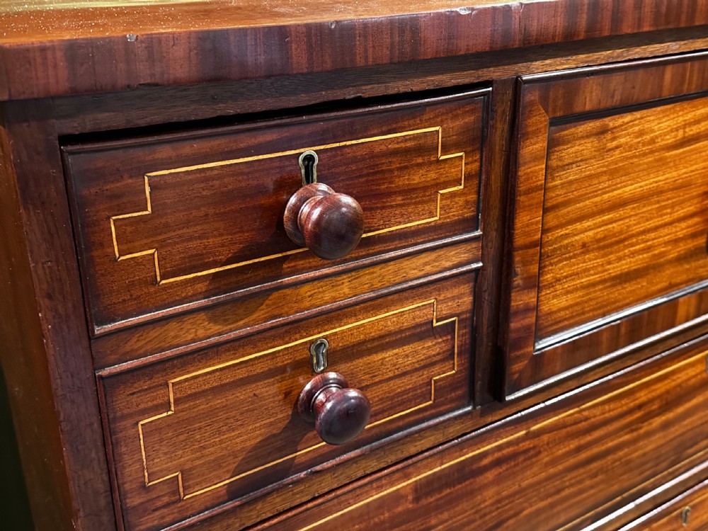 A Regency mahogany Scotch chest of drawers featuring boxwood inlay, a deep central drawer with a brass lion head pull, and multiple outer drawers with turned wooden knobs. View IV