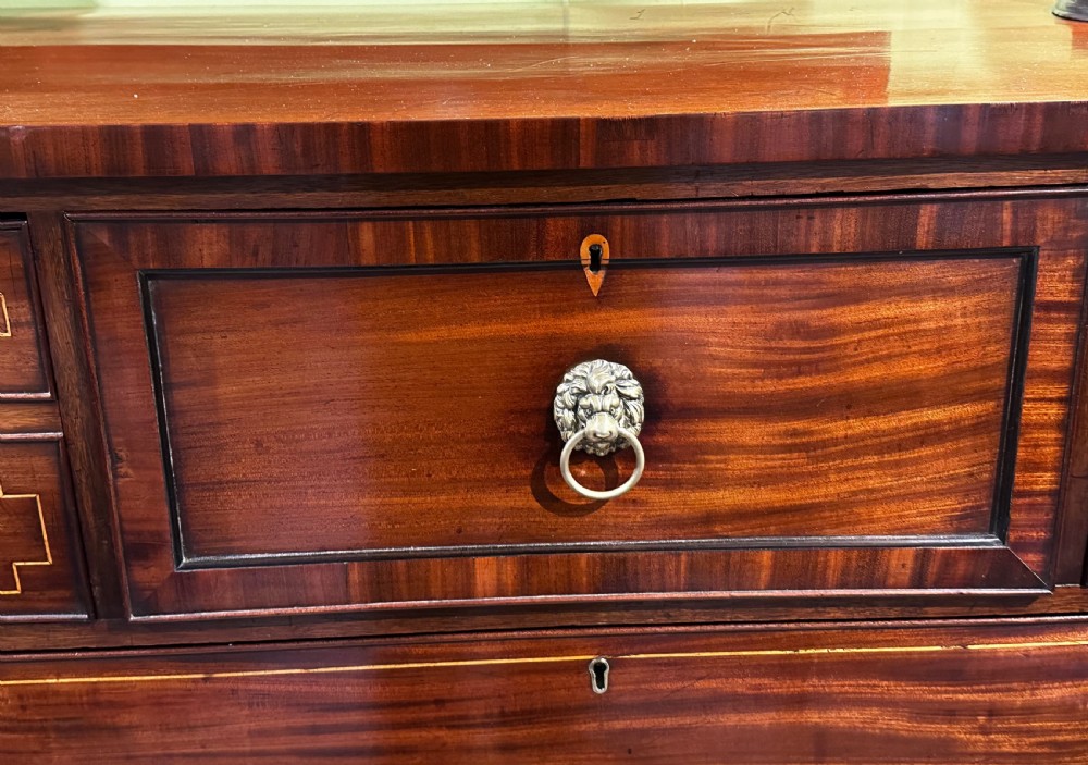 A Regency mahogany Scotch chest of drawers featuring boxwood inlay, a deep central drawer with a brass lion head pull, and multiple outer drawers with turned wooden knobs. View V
