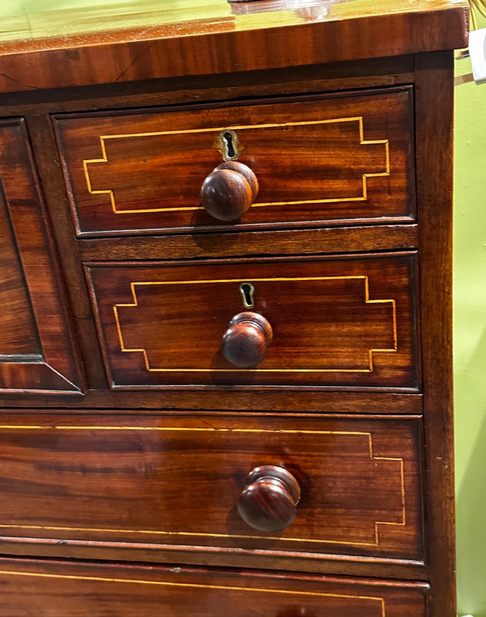 A Regency mahogany Scotch chest of drawers featuring boxwood inlay, a deep central drawer with a brass lion head pull, and multiple outer drawers with turned wooden knobs. View VI