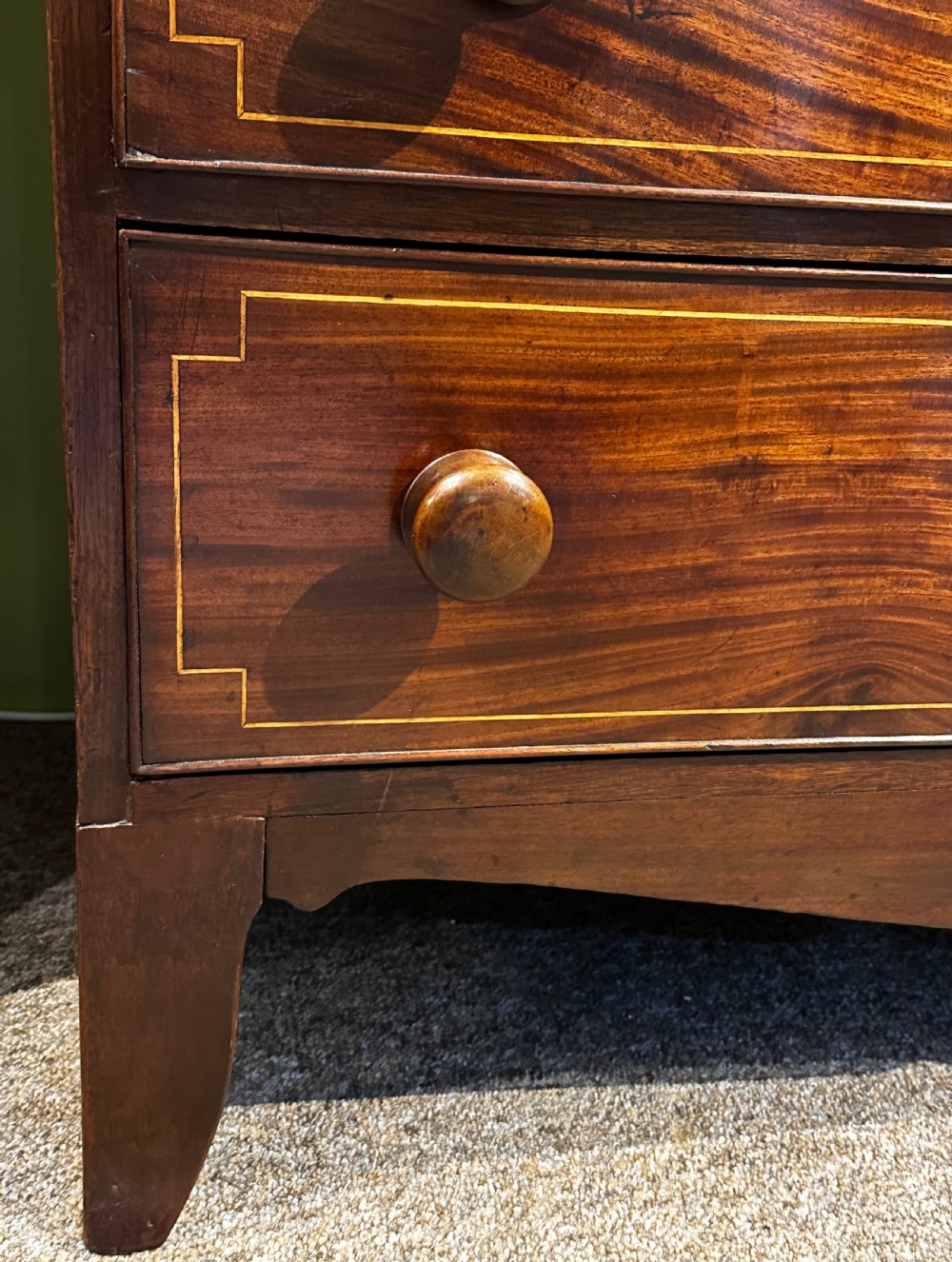 A Regency mahogany Scotch chest of drawers featuring boxwood inlay, a deep central drawer with a brass lion head pull, and multiple outer drawers with turned wooden knobs. View VIII
