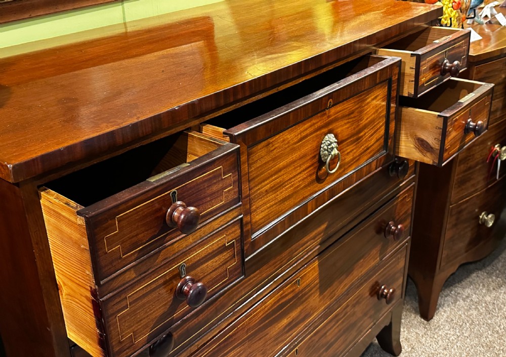 A Regency mahogany Scotch chest of drawers featuring boxwood inlay, a deep central drawer with a brass lion head pull, and multiple outer drawers with turned wooden knobs. View IX