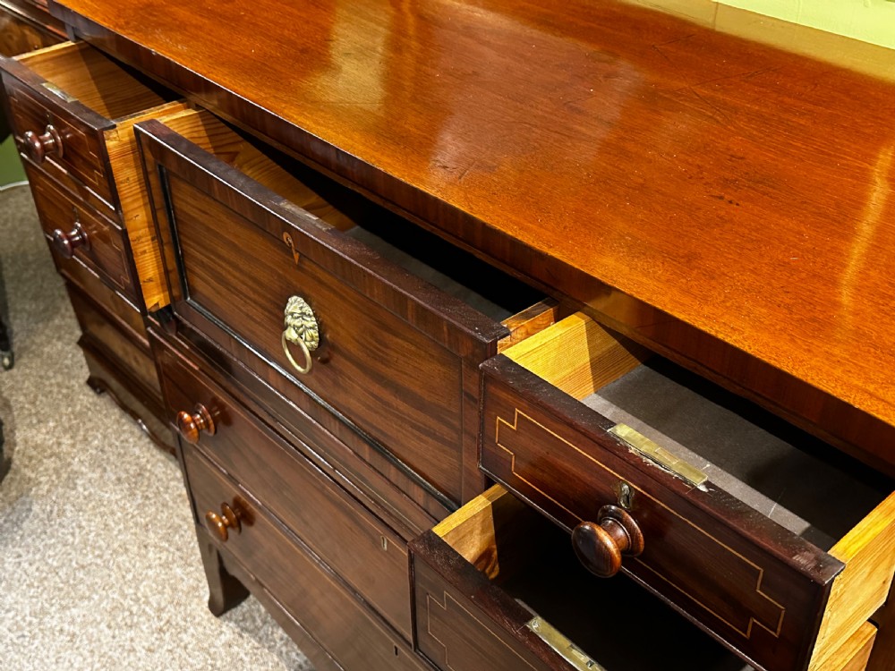 A Regency mahogany Scotch chest of drawers featuring boxwood inlay, a deep central drawer with a brass lion head pull, and multiple outer drawers with turned wooden knobs. View X