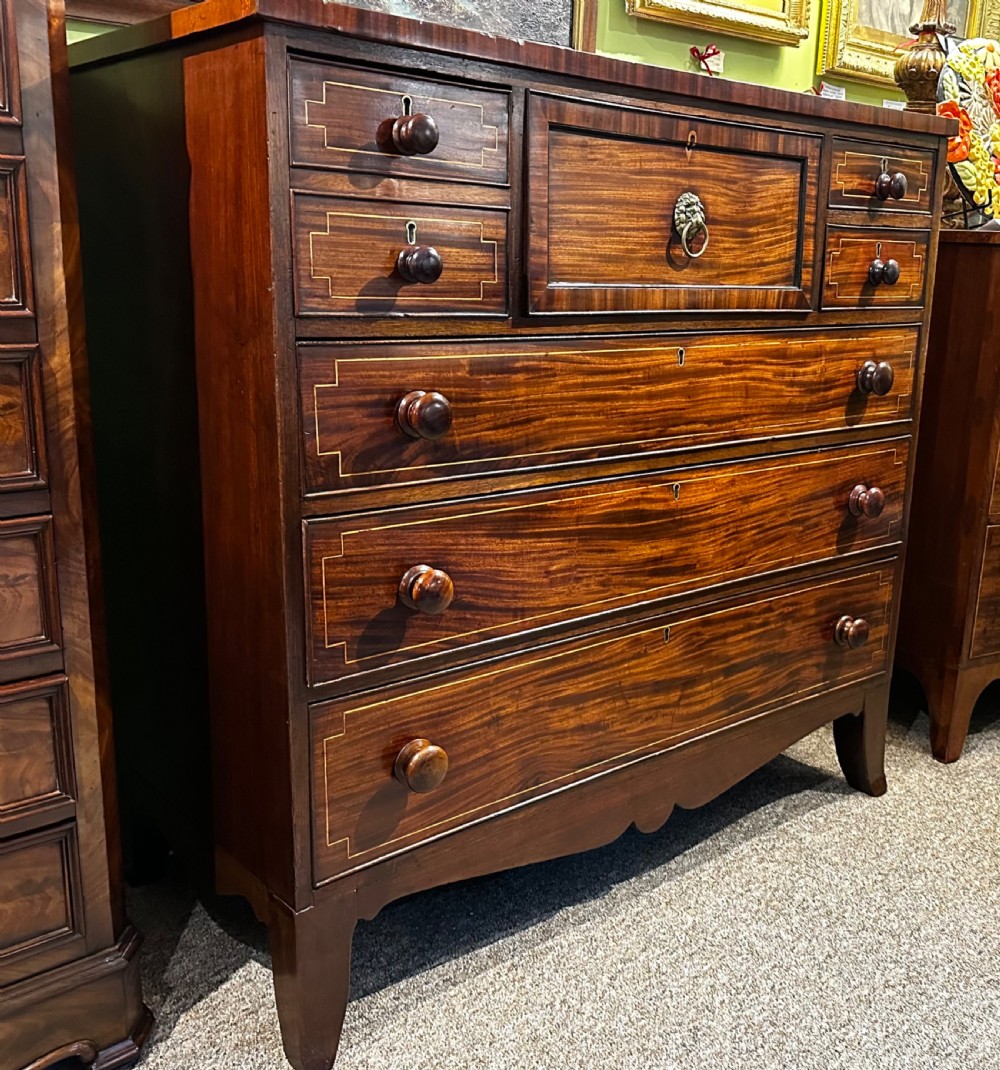 A Regency mahogany Scotch chest of drawers featuring boxwood inlay, a deep central drawer with a brass lion head pull, and multiple outer drawers with turned wooden knobs. View XII