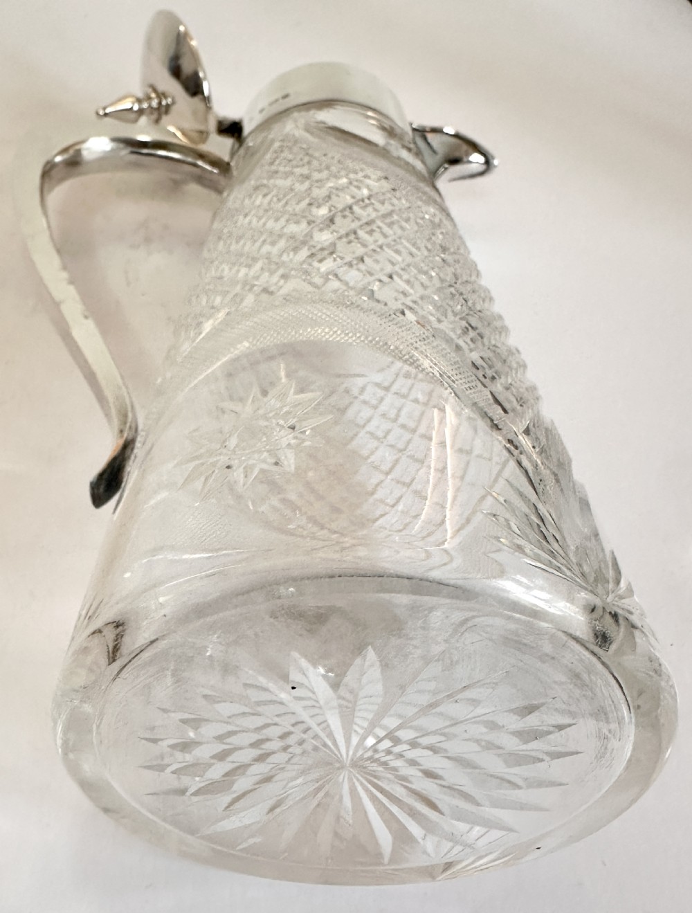 A tall cut glass claret jug decorated with diamond cut facets, featuring a polished silver-plated collar, hinged lid with finial, and an angular handle. View VIII