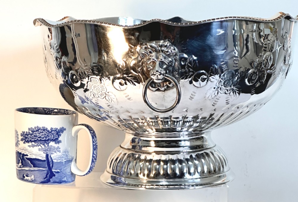 A silver-plated pedestal punch bowl featuring embossed floral repousse decoration, a scalloped rim, and twin lion mask drop-ring handles. View II