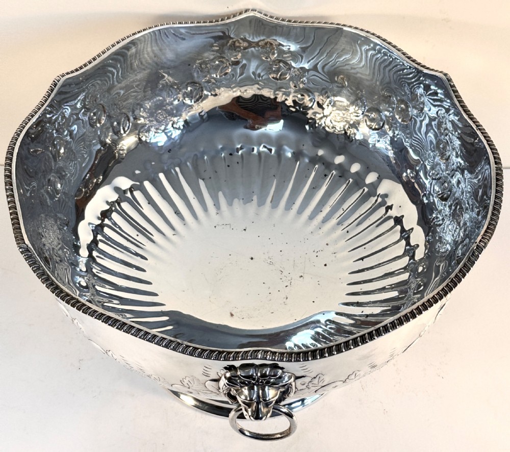 A silver-plated pedestal punch bowl featuring embossed floral repousse decoration, a scalloped rim, and twin lion mask drop-ring handles. View III