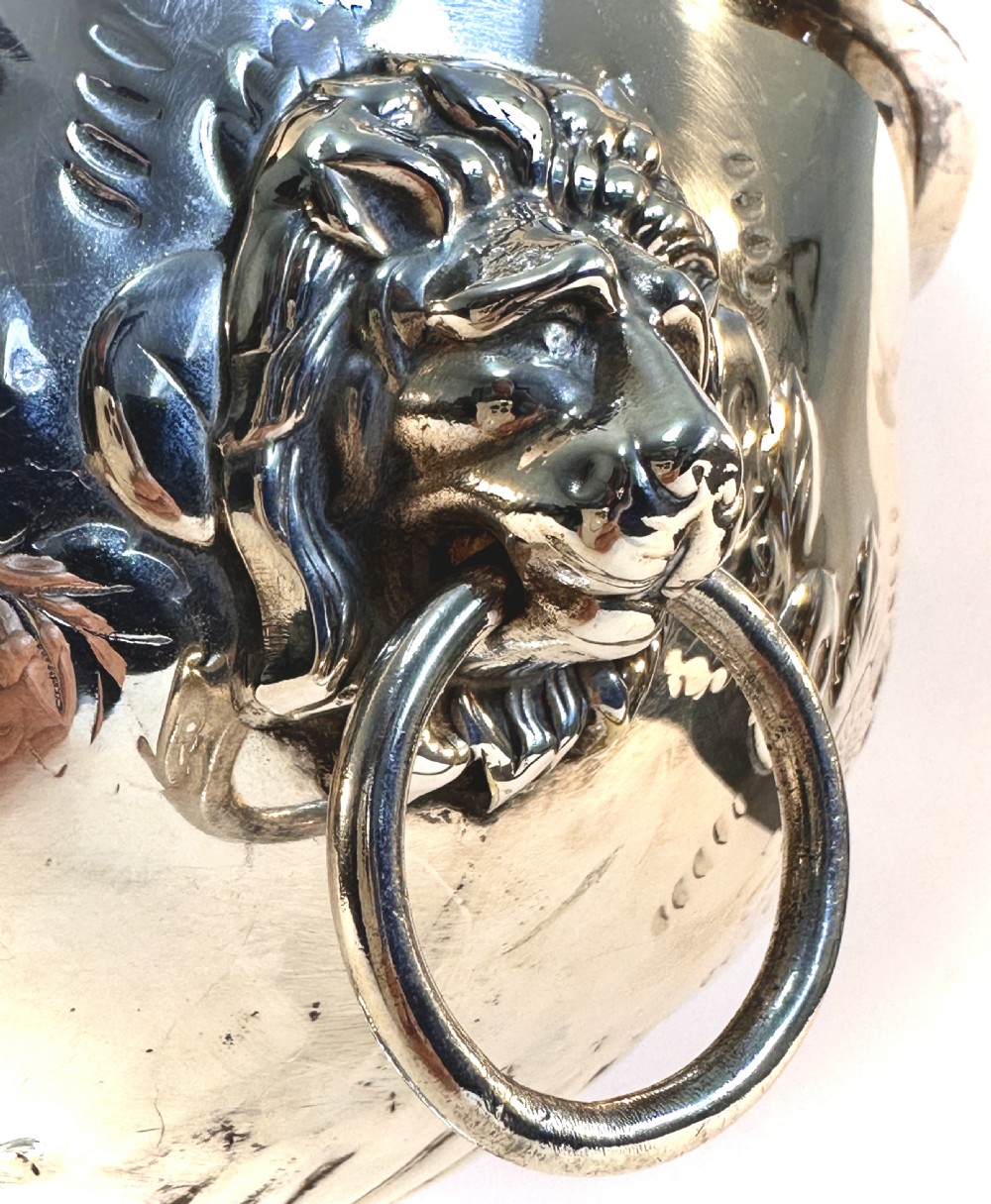 A silver-plated pedestal punch bowl featuring embossed floral repousse decoration, a scalloped rim, and twin lion mask drop-ring handles. View IX