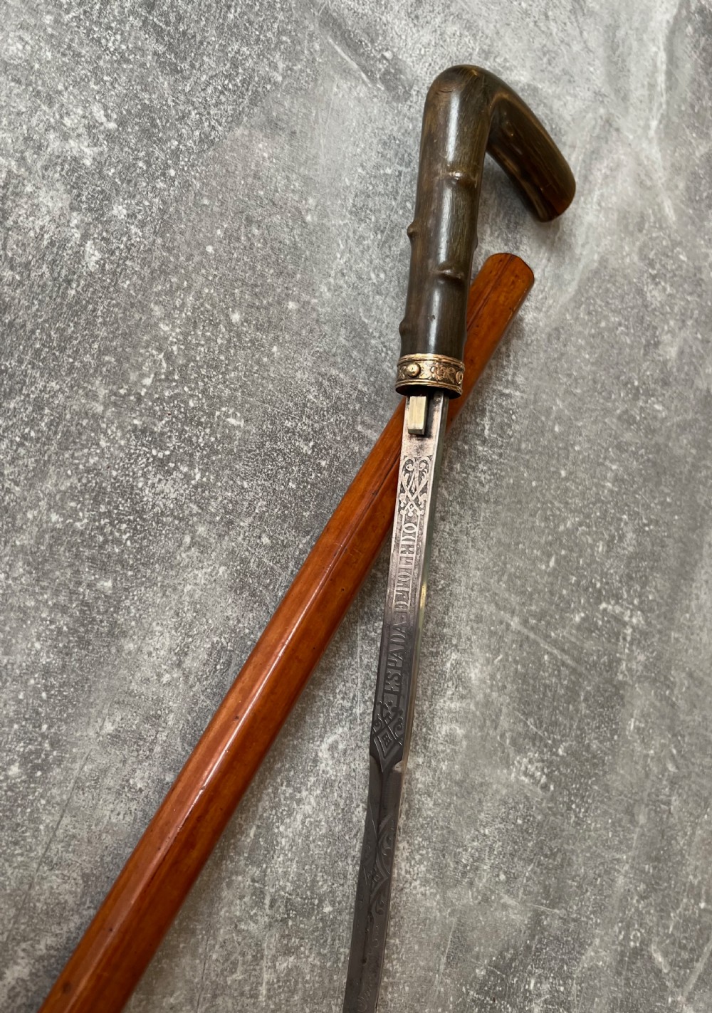 An antique malacca wood sword stick featuring a curved horn handle, decorative brass collar with push button release, and an etched steel Toledo blade.