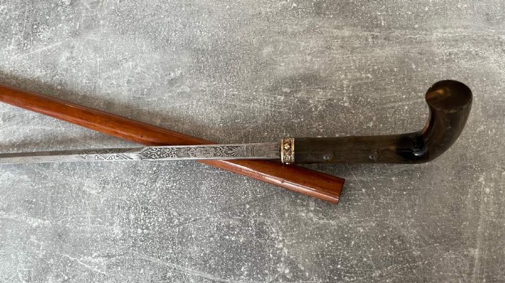 An antique malacca wood sword stick featuring a curved horn handle, decorative brass collar with push button release, and an etched steel Toledo blade. View VI