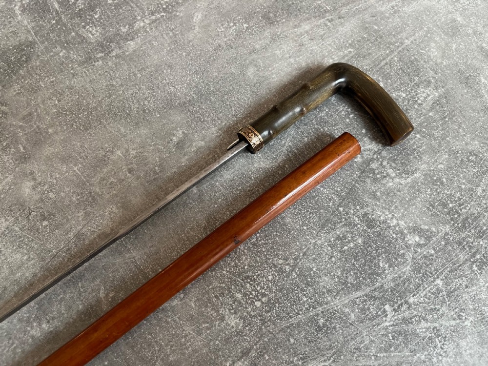 An antique malacca wood sword stick featuring a curved horn handle, decorative brass collar with push button release, and an etched steel Toledo blade. View IX