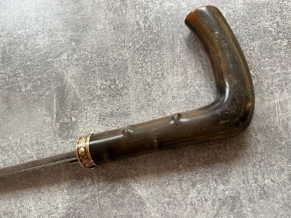 An antique malacca wood sword stick featuring a curved horn handle, decorative brass collar with push button release, and an etched steel Toledo blade. View X