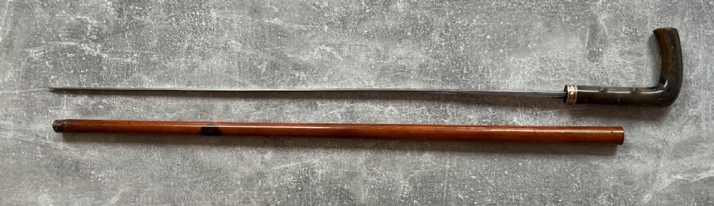 An antique malacca wood sword stick featuring a curved horn handle, decorative brass collar with push button release, and an etched steel Toledo blade. View XIII