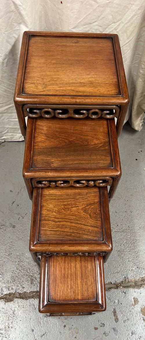A set of four graduated brown Chinese hardwood nesting tables featuring carved scroll aprons and floating panel tops. View II