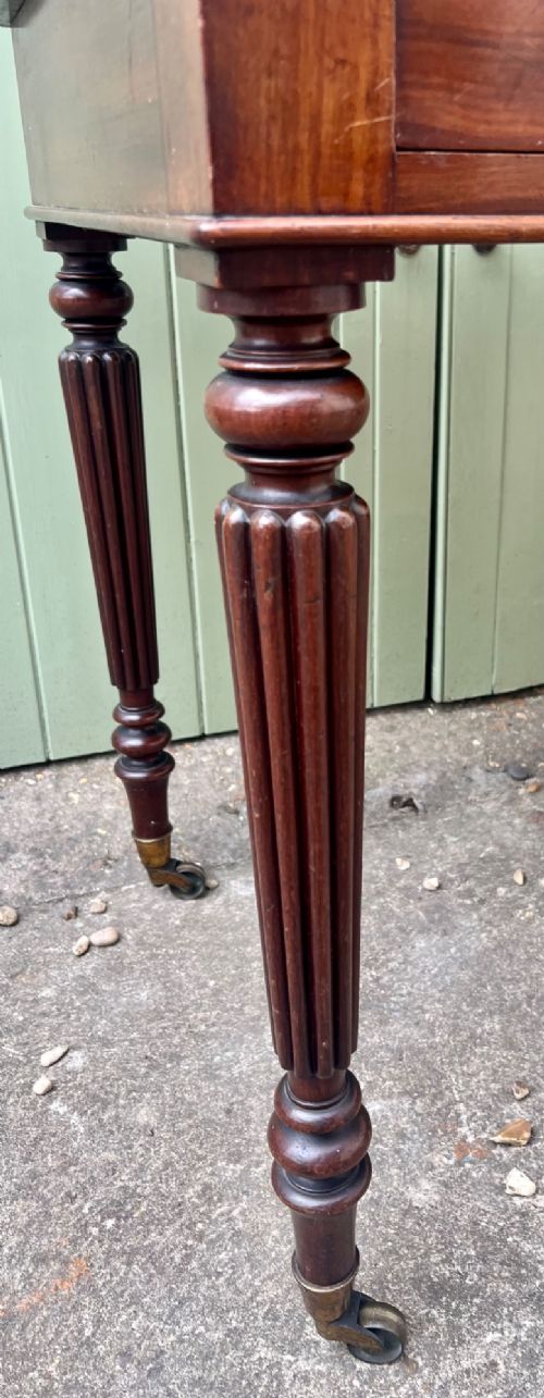 A nineteenth-century mahogany side table with a low gallery back, two frieze drawers, and turned reeded legs on brass castors. View IV