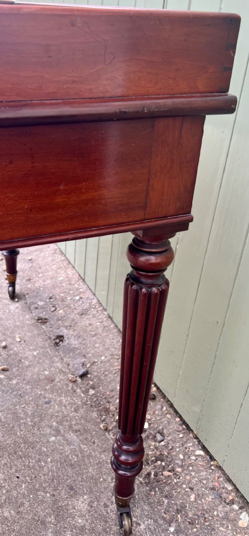 A nineteenth-century mahogany side table with a low gallery back, two frieze drawers, and turned reeded legs on brass castors. View V