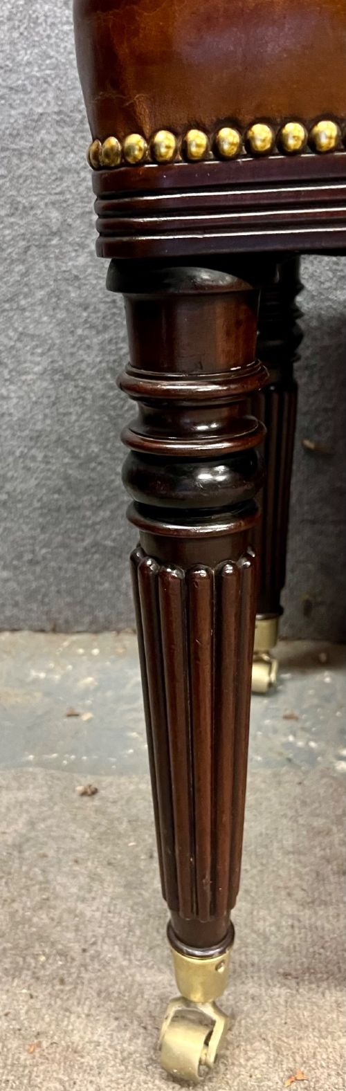 An early nineteenth-century upholstered brown leather bench featuring brass studded trim and six dark wood fluted turned legs on brass castors. View IV