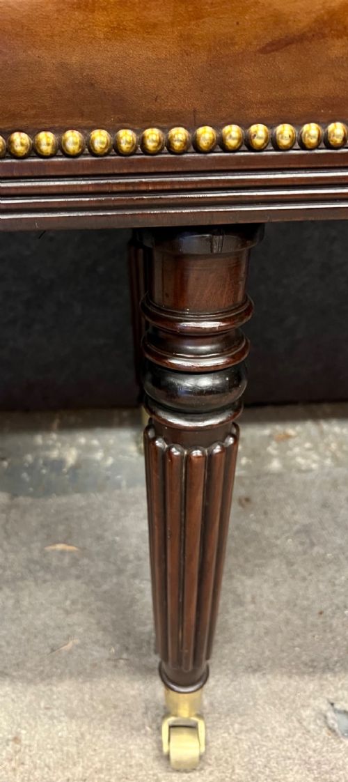 An early nineteenth-century upholstered brown leather bench featuring brass studded trim and six dark wood fluted turned legs on brass castors. View V