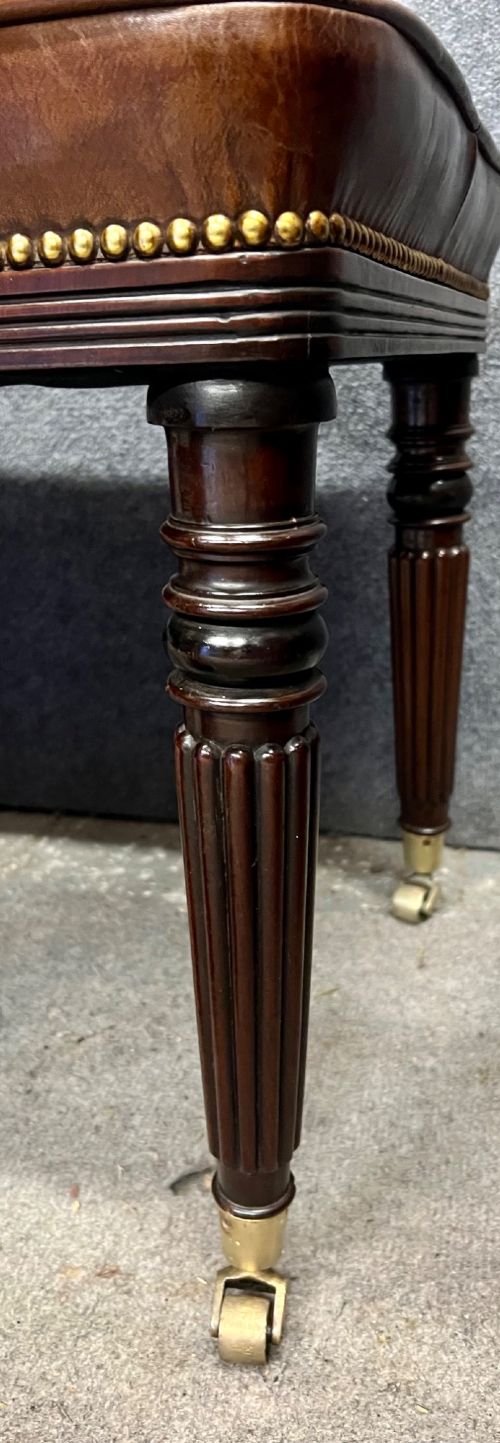 An early nineteenth-century upholstered brown leather bench featuring brass studded trim and six dark wood fluted turned legs on brass castors. View VI