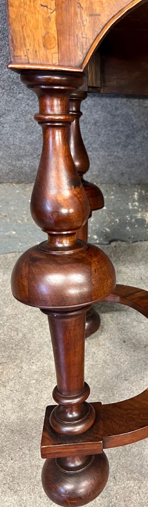 A William and Mary style walnut lowboy table featuring a quartered figured veneer top, a single drawer with brass drop handles, a shaped apron, turned legs, and a serpentine stretcher. View VIII