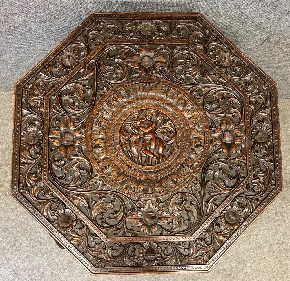 An octagonal dark brown teak coffee table supported by four intricately carved elephant legs with upturned trunks and tusks, featuring an elaborately carved floral top surface. View III