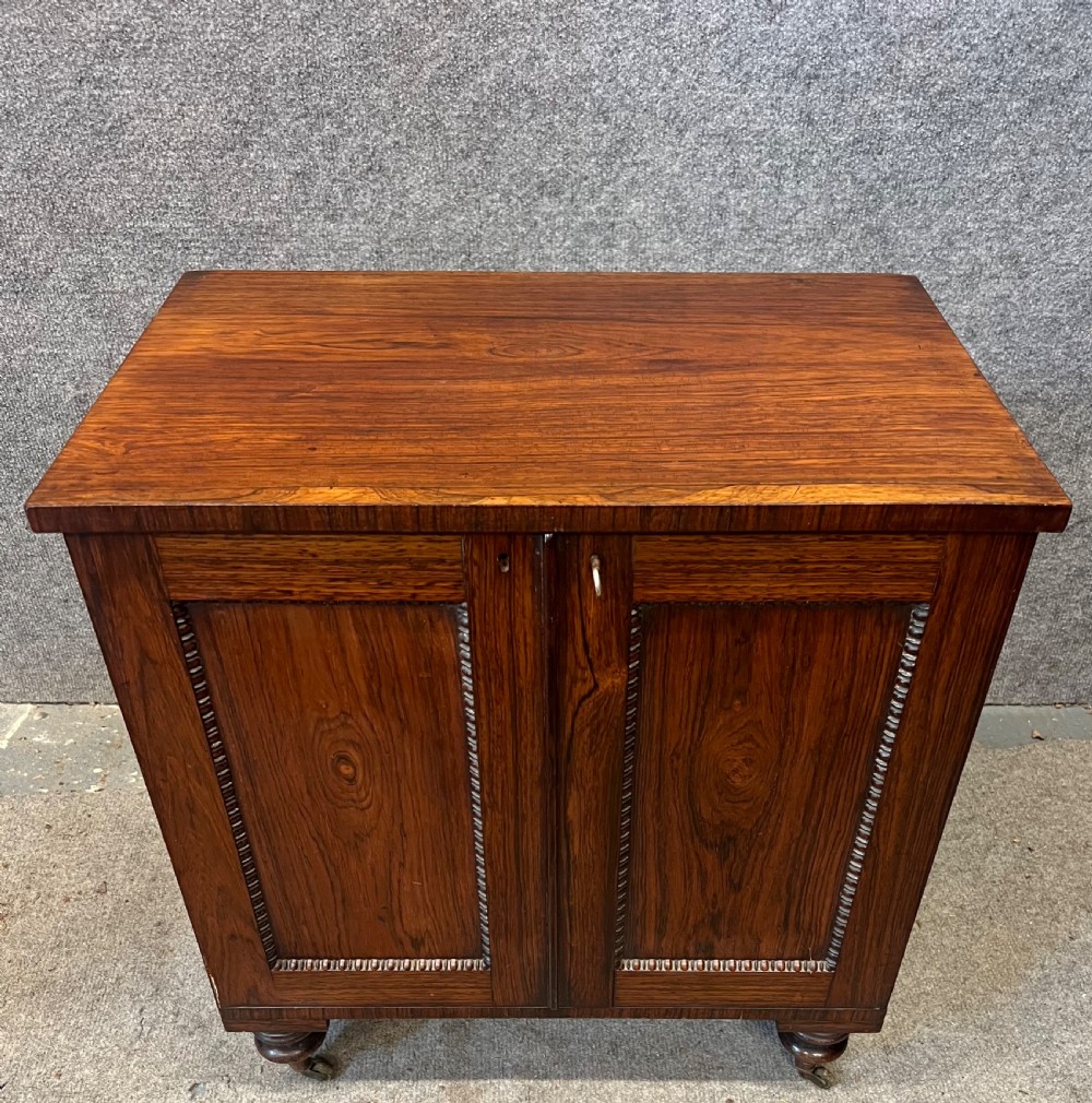 A low rectangular antique rosewood cellarette cabinet with twin panelled doors framed by beaded moulding, resting on turned feet with brass castors.