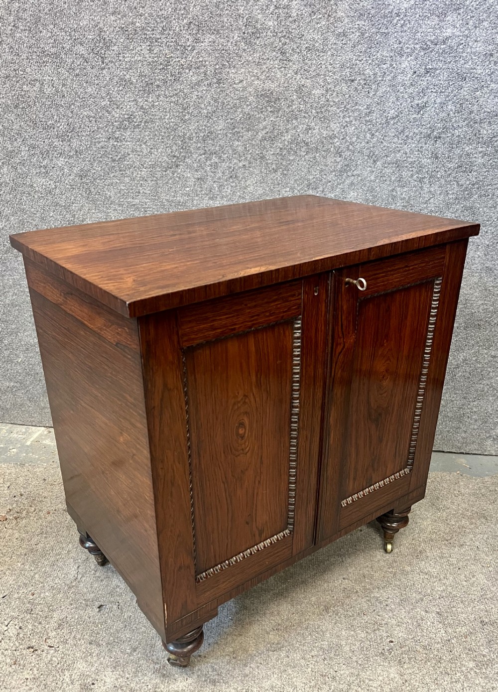 A low rectangular antique rosewood cellarette cabinet with twin panelled doors framed by beaded moulding, resting on turned feet with brass castors. View IV