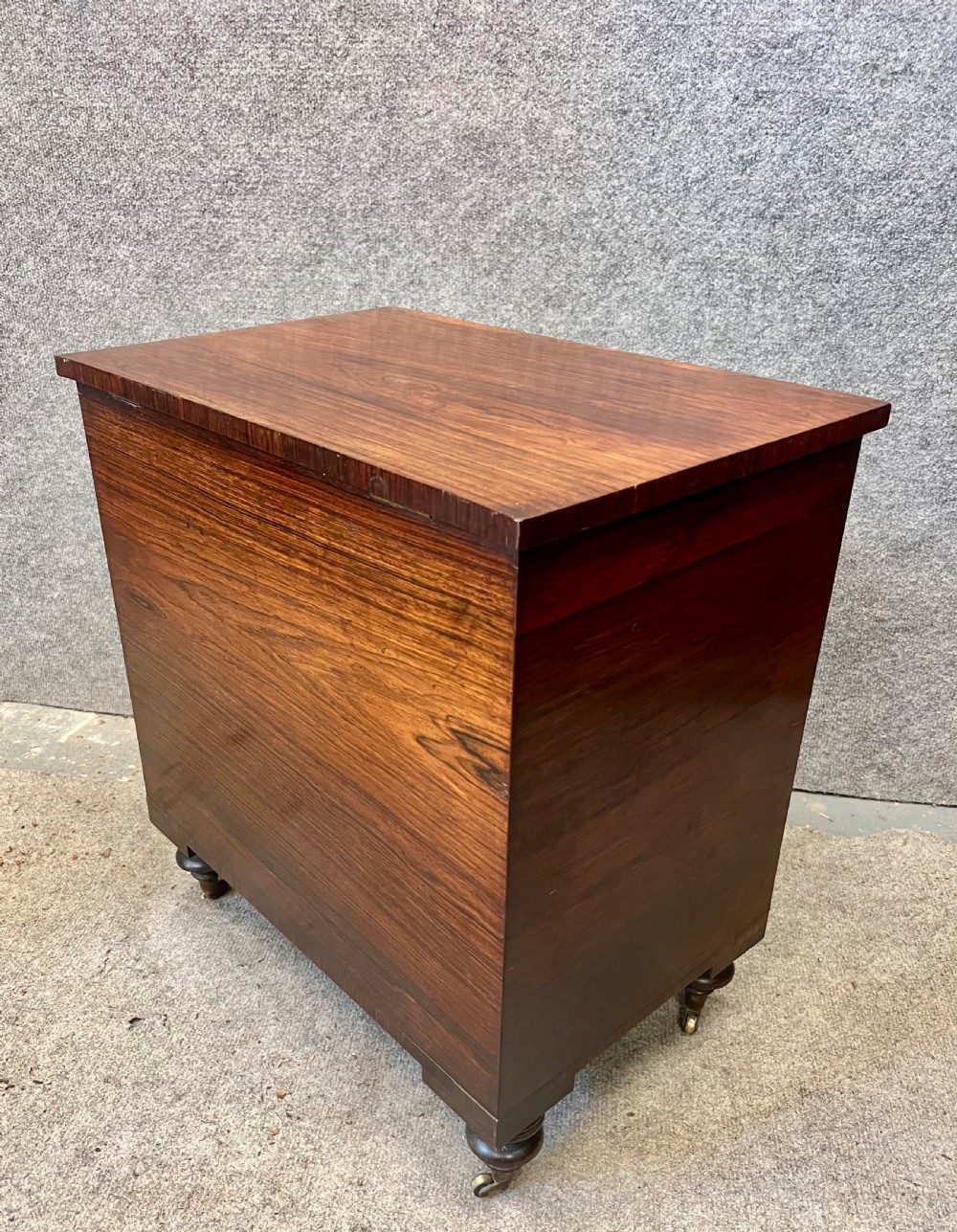 A low rectangular antique rosewood cellarette cabinet with twin panelled doors framed by beaded moulding, resting on turned feet with brass castors. View V