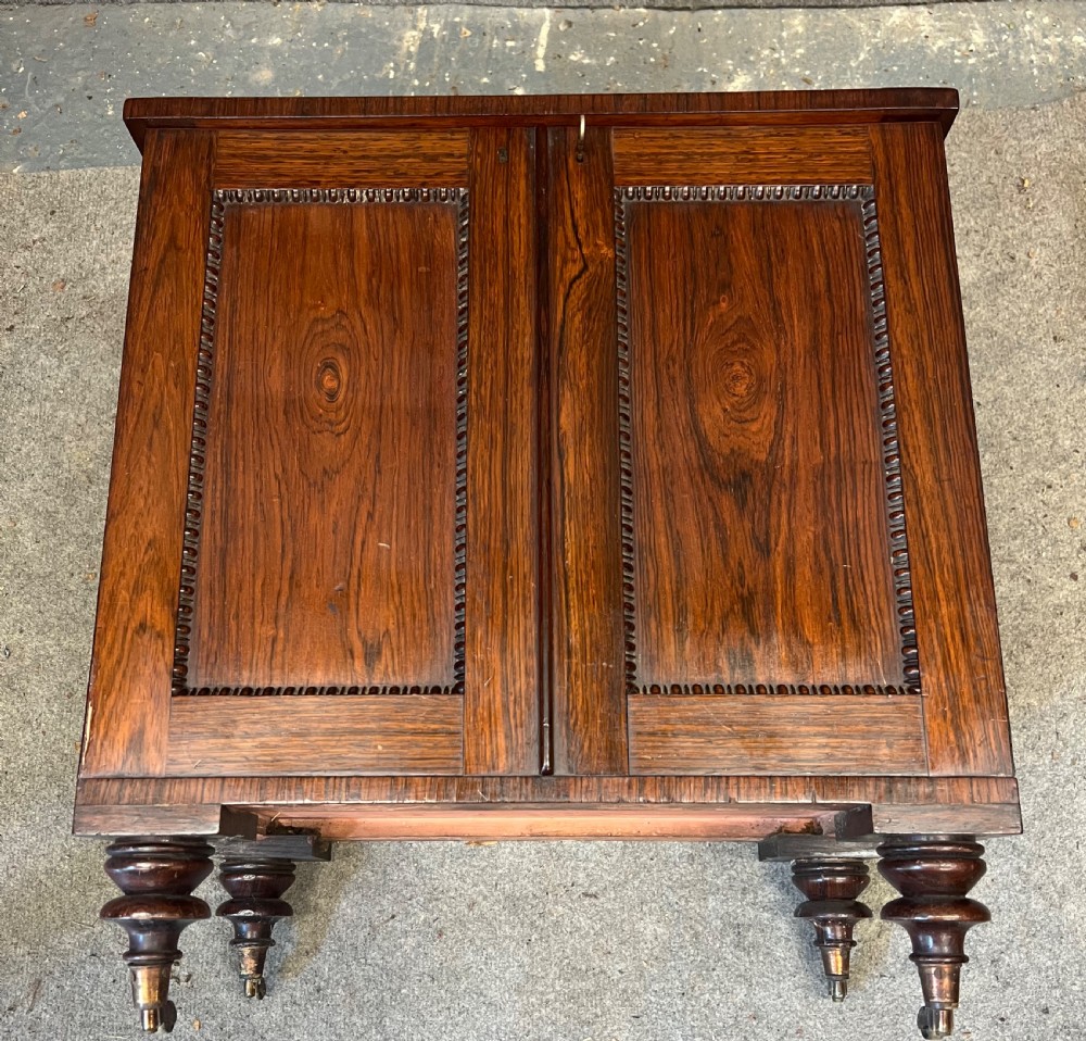 A low rectangular antique rosewood cellarette cabinet with twin panelled doors framed by beaded moulding, resting on turned feet with brass castors. View VII
