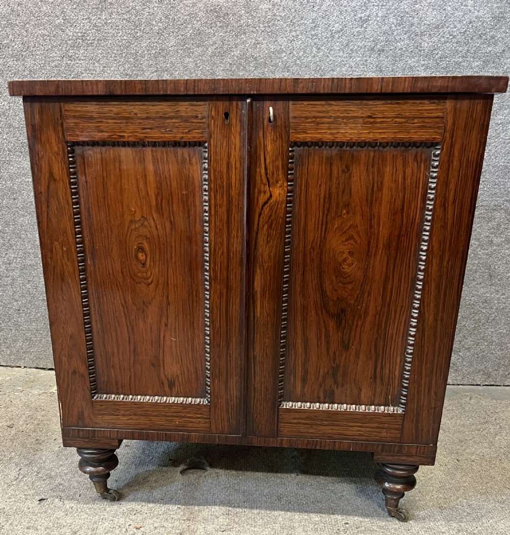 A low rectangular antique rosewood cellarette cabinet with twin panelled doors framed by beaded moulding, resting on turned feet with brass castors. View VIII