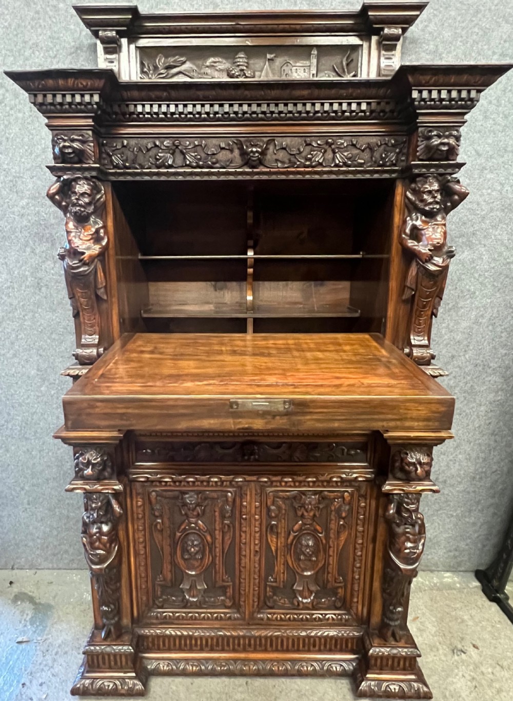 A heavily carved dark walnut cabinet featuring figurative reliefs, caryatid supports, mask motifs, and an architectural cresting. View III