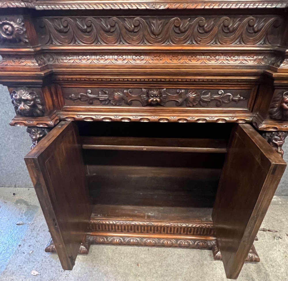 A heavily carved dark walnut cabinet featuring figurative reliefs, caryatid supports, mask motifs, and an architectural cresting. View IV