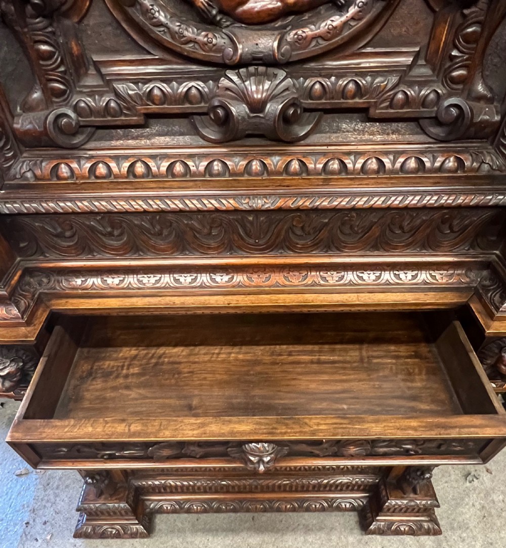 A heavily carved dark walnut cabinet featuring figurative reliefs, caryatid supports, mask motifs, and an architectural cresting. View V