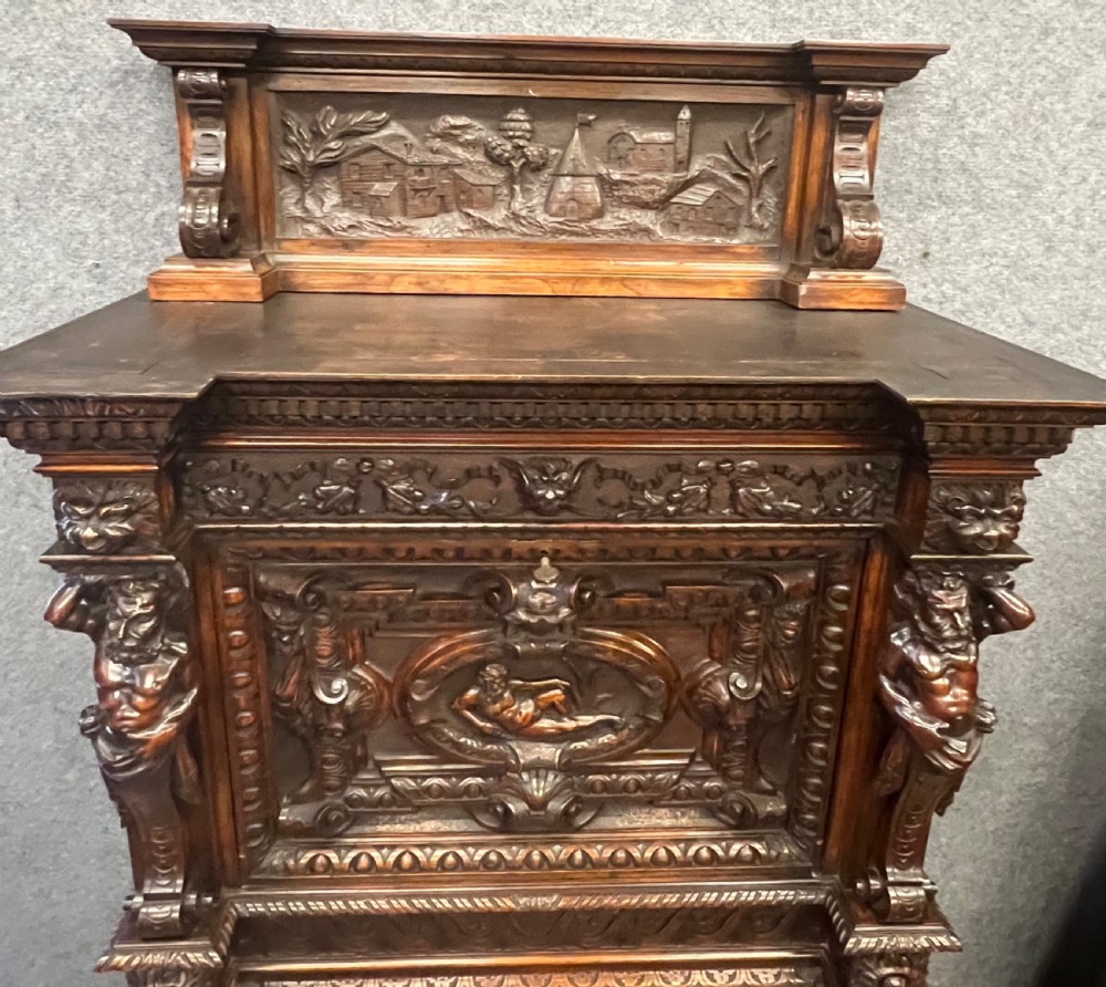 A heavily carved dark walnut cabinet featuring figurative reliefs, caryatid supports, mask motifs, and an architectural cresting. View IX