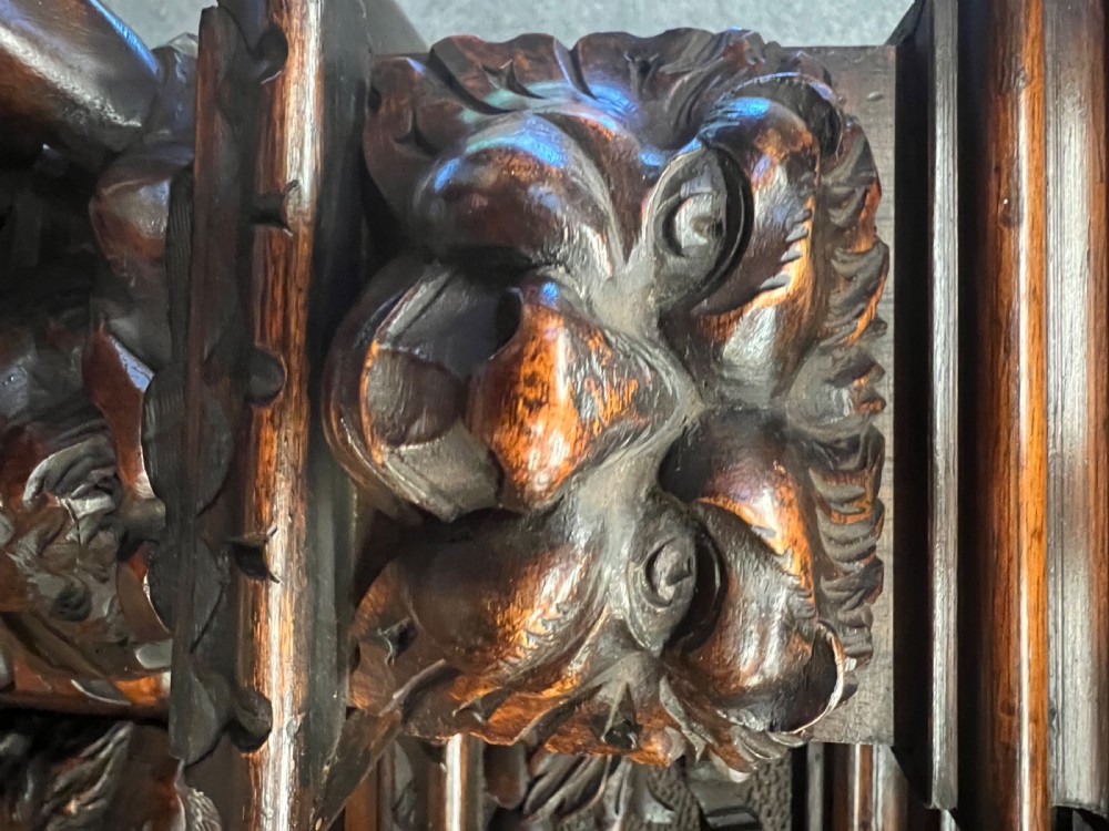A heavily carved dark walnut cabinet featuring figurative reliefs, caryatid supports, mask motifs, and an architectural cresting. View X